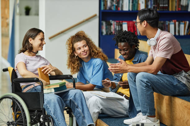 Students smiling sitting with one student in a wheelchair, at the library